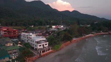 Dağların tepelerinde süzülen yumuşak pembe bulutlar sakin sahil şeridinde ve Tayland 'daki tropikal koh chang adasının el değmemiş sularında ılık günbatımı parlaklığı yaratır.