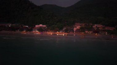 Gece sakin bir sahil manzarası aydınlık otelleri ve Tayland 'daki Koh Chang adasının tatil beldelerini gösteriyor. Karanlık gökyüzünün altındaki sakin okyanus suyuna yansıyor.