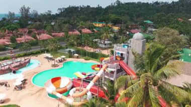 Yüksek slaytlı ve yüzme havuzlu bir su parkı. Tahttan parlak renkli slaytlara ve turkuaz su havuzuna kadar en üst manzara. İnsanlar yüzer, ata biner ve oynar. Her yerde ağaçlar ve palmiye ağaçları var.