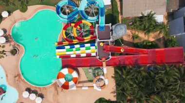 Yüksek slaytlı ve yüzme havuzlu bir su parkı. Tahttan parlak renkli slaytlara ve turkuaz su havuzuna kadar en üst manzara. İnsanlar yüzer, ata biner ve oynar. Her yerde ağaçlar ve palmiye ağaçları var.