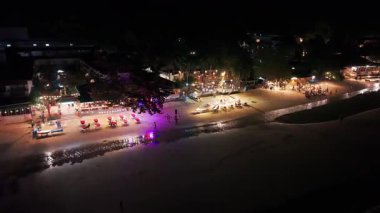 Lokanta teraslarının yakınındaki kumlu kıyı şeridini nazikçe okşayan ay ışığı dalgaları, turistlerin akşam vakti deniz manzarasında rahatça gezinmeleriyle