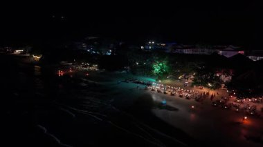 Gece kumsal partisi enerji dolu, turistlerin dans ettiği, canlı müziğin ve renkli aydınlanmanın tadını çıkardığı ve unutulmaz deniz kenarı atmosferi yarattığı bir parti.