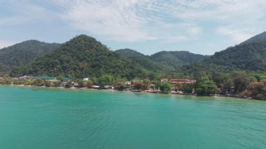 Koh Chang Adası tropikal kıyı şeridi turkuaz suyu, beyaz kumlu plajlar, yemyeşil orman dağları ve bulutlu bir gökyüzünün altındaki otelleri sunar.