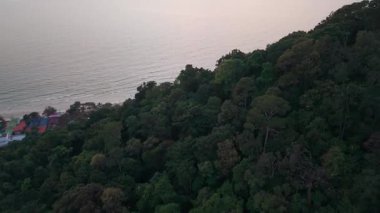 Sakin okyanus suyunun üzerinde pembe günbatımı, kumlu sahile yaklaşan güneş ışığını yansıtıyor ve Koh Chang Adası 'ndaki tatil merkezlerinin arkasındaki yamaçta tropikal yağmur ormanları var.