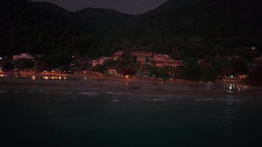 Renkli ışıklar, Tayland 'daki Koh Chang Adası' ndaki sahil otelleri ve restoranları aydınlatarak orman dağlarının karanlık zeminine karşı canlı bir gece hayatı sahnesi yaratıyor.