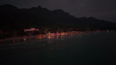 Gece aydınlanması Koh Chang kıyı şeridinde parıldıyor, sakin deniz sularına karanlık alacakaranlık gökyüzünün altında canlı yansımalar yapıyor.