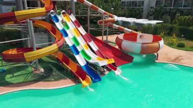 Yüksek slaytlı ve yüzme havuzlu bir su parkı. Tahttan parlak renkli slaytlara ve turkuaz su havuzuna kadar en üst manzara. İnsanlar yüzer, ata biner ve oynar. Her yerde ağaçlar ve palmiye ağaçları var.