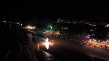 Kalabalık plajı aydınlatan canlı bir dolunay partisi, göz kamaştırıcı kıvılcımlarla gece gökyüzünü aydınlatan havai fişekler, renkli enerji ve heyecanı yansıtan şenlikli kutlamalar.