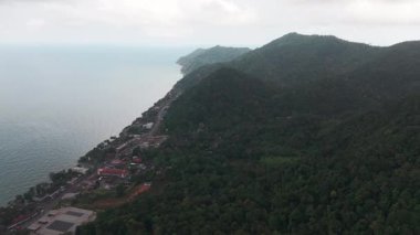 Koh Chang adasının kıyı şeridi açık mavi deniz ile canlı yeşil tropikal orman arasında bulutlu bir gökyüzünün altında güzel bir kontrastlık sergiliyor.