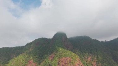 Verdant dağ yamaçları yoğun tropikal ormanlarla örtülmüş, bulutlu gökyüzünün altında uzanan katmanlı yeşil tepeleri ortaya çıkarıyor, el değmemiş vahşi doğayı gözler önüne seriyor.