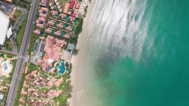 Sakin turkuaz okyanus dalgaları canlı bir sahil beldesinin yanındaki kumlu sahili nazikçe okşayarak rahatlama ve rahatlama manzarası yaratıyor.