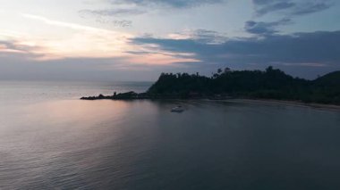 Sakin okyanus sularında altın gün batımının yansımalarını barındıran sakin tropikal deniz manzarası sakin akşam ışığı sırasında yemyeşil ada kıyılarına demirlemiş küçük bir yat.