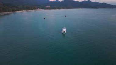 Sakin günbatımı feribotu sakin tropikal sularda yüzüyor, yemyeşil ada dağları akşam gökyüzüne karşı siluetlenmiş, dingin deniz manzarası yaratıyor.