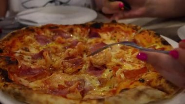 Kadın elleri dikkatle kesiyor ve taze pişmiş pizza dilimlerini beyaz tabağa servis ediyor, İtalyan mutfağında leziz bir yemek deneyimi sergiliyor.