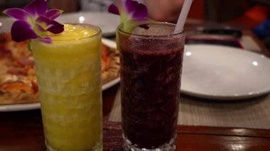 Ispanak, jambon ve peynir gibi taze malzemelerle süslenmiş gurme pizzalar, kırsal ahşap restoran masasında orkide çiçekleriyle süslenmiş canlı meyve sularının yanında oturur.