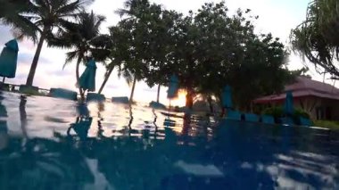 Şatafatlı sonsuz havuz, altın güneş ışığını yansıtıyor. Palmiye ağaçları ve şemsiyeler el değmemiş tatil köylerinde sakin tropikal manzaralar yaratıyor.