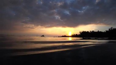 Sıcak altın saat güneş ışığı yumuşak okyanus yüzeyine yansıyor, sakin deniz manzarasına karşı yumuşak ufkuyla uzak yelkenli tekneyi ortaya çıkarıyor.