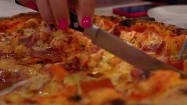 Kadın elleri dikkatle kesiyor ve taze pişmiş pizza dilimlerini beyaz tabağa servis ediyor, İtalyan mutfağında leziz bir yemek deneyimi sergiliyor.