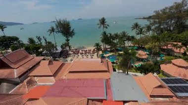 Hava manzarası turkuaz suları yakalıyor, güneş panelli çatısı, yüzme havuzu ve tropik cenneti çerçeveleyen bereketli palmiye ağaçları olan lüks sahil otelini çevreleyen el değmemiş beyaz kumlu plajlar.