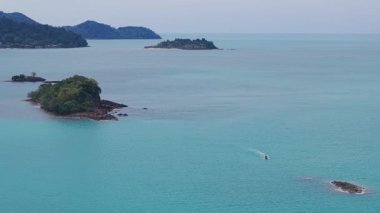 Kristal berrak turkuaz su, bereketli bitki örtüsüyle kaplı küçük, kayalık bir adanın çevresini sarar.