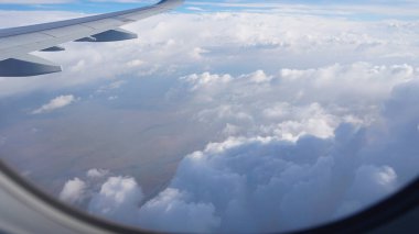 Bir uçak penceresinden nefes kesici bir görüntü yakalamak, yemyeşil alanlar ve kabarık beyaz bulutların yanında kanadı göstermek, uçuş sırasında nefes kesici bir hava perspektifi sunuyor.