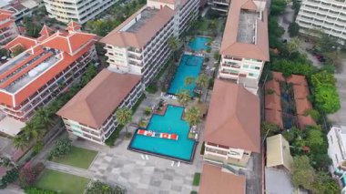 Palmiye ağaçları ve otel binalarıyla çevrili tropikal bir tatil köyünde yüzen ve havuzda oynayan turistlerin manzarası arttı.