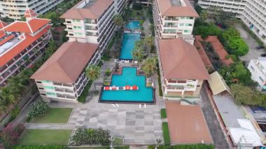 Şişme oyuncaklar, geleneksel Asya mimarisi ve palmiye ağaçları ve diğer binalarla çevrili tropikal bir tatil köyünün havuzunda yavaş yavaş beliriyor.