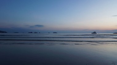 Güneş batarken, turistler tropikal bir okyanusun yumuşak dalgalarının tadını çıkarıyorlar. Ufuk ve adaları süsleyen tekneler huzur dolu manzaraya biraz huzur katıyor.