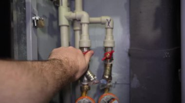 Tamirci, rutin tesisat onarımı sırasında iki turuncu elektrik sayacının yanına yerleştirilmiş beyaz plastik su borusundaki kırmızı vanayı dikkatlice çeviriyor.