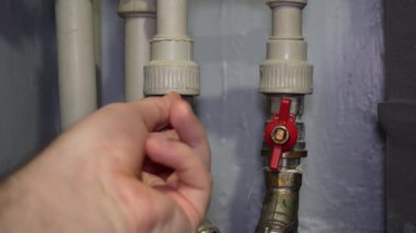 Profesyonel tesisatçı yerli su ısıtma sistemi borularının kırmızı valflerini dikkatlice çeviriyor, bakım servisi sırasında boru hattı bağlantılarını hassasiyetle yönetiyor.