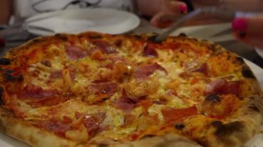Kadın elleri dikkatle kesiyor ve taze pişmiş pizza dilimlerini beyaz tabağa servis ediyor, İtalyan mutfağında leziz bir yemek deneyimi sergiliyor.