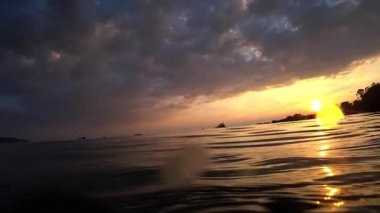 Altın gün batımı ılık renklere bürünüyor ve sakin okyanus sularına yansıyor. Uzak kayıklar bulutlu gökyüzüne karşı huzur içinde ilerliyor.