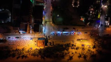 Sahildeki yol boyunca vızıldayan aydınlatılmış gece pazarında, sokak satıcıları tropikal akşam arkaplanına karşı siluetlenmiş palmiye ağaçlarının arasında yerel mutfağı hazırlıyorlar.