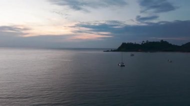 Altın ışıklı banyo yapan sakin yelkenliler manzaralı kıyı şeridinde dinleniyor, nefes kesen akşam alacakaranlığı boyunca canlı gökyüzü renkleriyle sakin deniz manzarası sergiliyor.