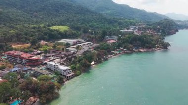 Tayland 'daki Koh Chang Adası, tropikal yeşilliklerin ortasında renkli kıyı binalarının yuva yaptığı turkuaz sularla buluşmak için çağlayan yeşil orman manzarası sunar.