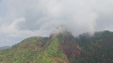 Verdant dağ yamaçları yoğun tropikal ormanlarla örtülmüş, bulutlu gökyüzünün altında uzanan katmanlı yeşil tepeleri ortaya çıkarıyor, el değmemiş vahşi doğayı gözler önüne seriyor.