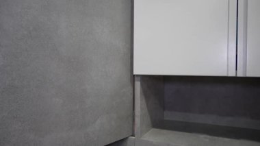 Profesyonel müteahhit, banyo yenileme sırasında büyük formatta gri seramik fayans yerleştiriyor. Uzman hassasiyetine sahip beyaz banyo armatürlerinin yanına yerleştirilmiş fayanslar.