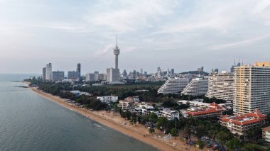 Alacakaranlıkta pattaya sahilinin tadını çıkaran turistler, kıyı şeridine hakim olan şehir siluetinin sakin denizle buluşması karşısında nefes kesici bir manzara sunuyorlar.