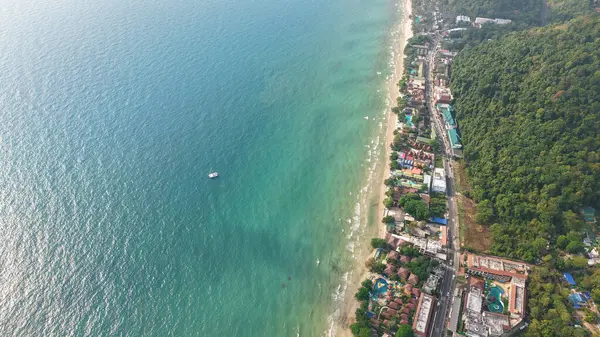 Nefes kesen hava perspektifi canlı bir tropikal plaj ve yemyeşil bir ormanın ahenkli bir buluşmasını yakalıyor, doğanın huzur dolu güzelliğini sergiliyor. Resimli bir sahil şeridi boyunca sarılıyor.