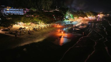 Tayland 'da tropikal bir plajda hayat dolu bir gece sahnesi başlıyor. Turistler yemek yerken. Sosyalleşiyorum. Işıkların ve meşalelerin altında ateş gösterilerini izliyordum. Canlı ve şenlikli bir atmosfer yaratıyor.