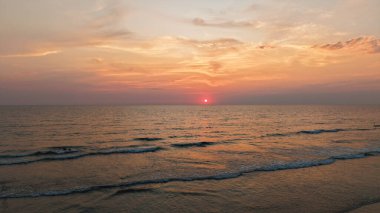 Gün batımında kıyıya vuran hafif dalgalar huzur, rahatlama ve doğanın güzelliğini temsil etmek için mükemmel sakin ve resimsel bir sahne yaratıyor.