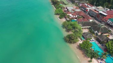 Turkuaz su, Tayland 'ın Koh Chang adasındaki verimli tropikal bitki örtüsüyle karşılaşırken, turistler de yüzme ve güneşlenmenin keyfini çıkarıyorlar.