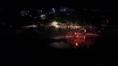 Gece sahili gösterisinde ateş dansçıları büyüleyici alevlerle performans sergiliyor, ıslak kumda parlak yansımalar yaratırken turistler de bayramlık tropikal kutlamalar sırasında hayranlıkla izliyorlar.
