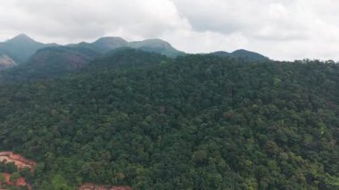 Verdant dağ manzarası denize doğru uzanıyor, engebeli araziyi kaplayan yoğun yağmur ormanı bulutlu gökyüzü yemyeşil çöllerin arasına yerleşmiş ıssız kıyı yerleşimlerini ortaya çıkarıyor.