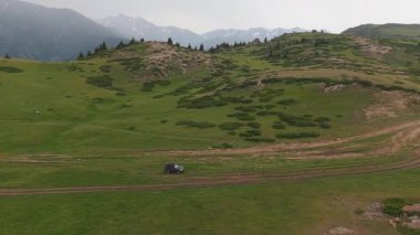 Yeşil çayırlar ve engebeli dağlar göz kamaştırıcı bir zemin sağlar. Bir off-road aracı virajlı toprak bir yolda yol alırken, sergilenen macera ve doğa keşifleri ile kucaklaşır.
