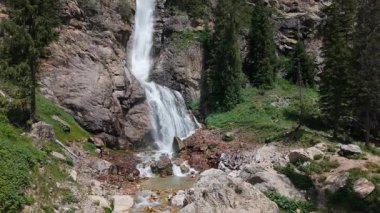 Güçlü şelale kayalıklardan aşağı düşüyor, yemyeşil dağ vadileri el değmemiş doğal manzarayı deneyimleyen canlı kırmızı ceketli yalnız yürüyüşçülerle el değmemiş el değmemiş yabanı gözler önüne seriyor.