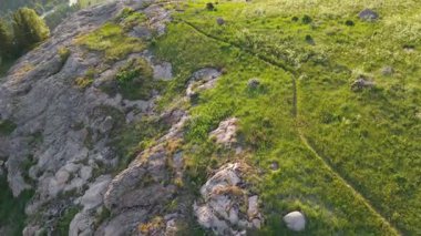 Bereketli yeşil bitki örtüsü bir dağ vadisinin dik yamaçlarını kaplıyor, aşağıdaki bir nehre doğru kıvrılan dar bir patika, etrafındaki arazinin genişliğini yavaş yavaş ortaya çıkarıyor.