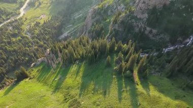 Sıcak güneş ışığı yemyeşil dağ vadisini aydınlatıyor, köşe bucak ağaç gölgelerinin altındaki kıvrımlı yolu ve nehri ortaya çıkarıyor altın saat manzara perspektifi boyunca