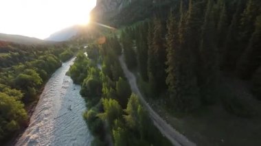 Güneş ışığı, akan bir nehir ve dolambaçlı toprak bir yolu olan el değmemiş bir dağ vadisini aydınlatır. Bu vadi, doğal güzelliğini ve sükunetini gözler önüne serer.