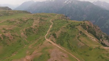 Serpentine dağ yolları yemyeşil çayırlar arasında zikzak çiziyor. Huzurlu vahşi doğa keşifleri sırasında dramatik bulutlu gökyüzünün altındaki görkemli dağlık tepeleri gözler önüne seriyor.